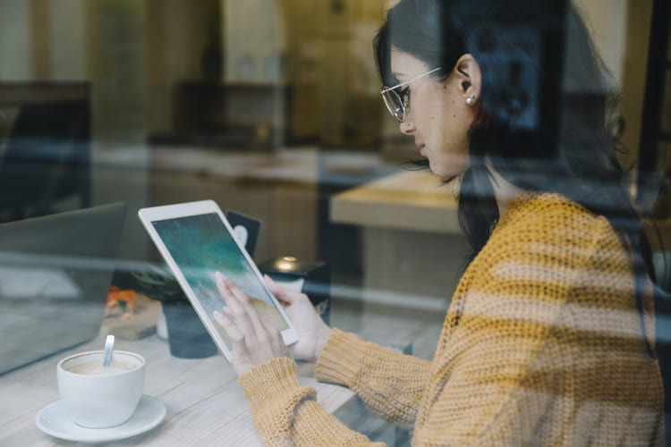 コーヒーを飲みながらタブレットを触る女性